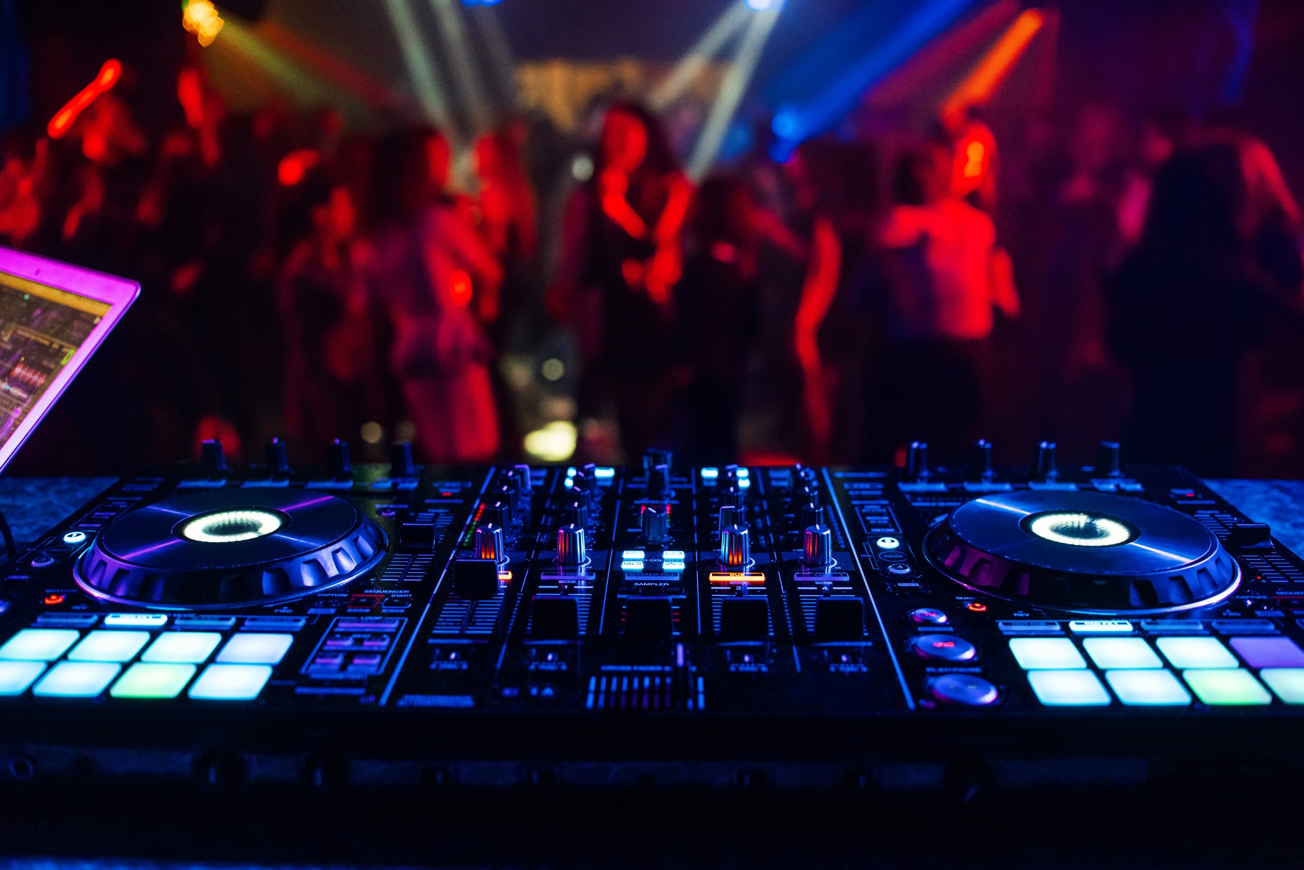 DJ mixer in a nightclub at a party with blurred silhouettes of dancing people
