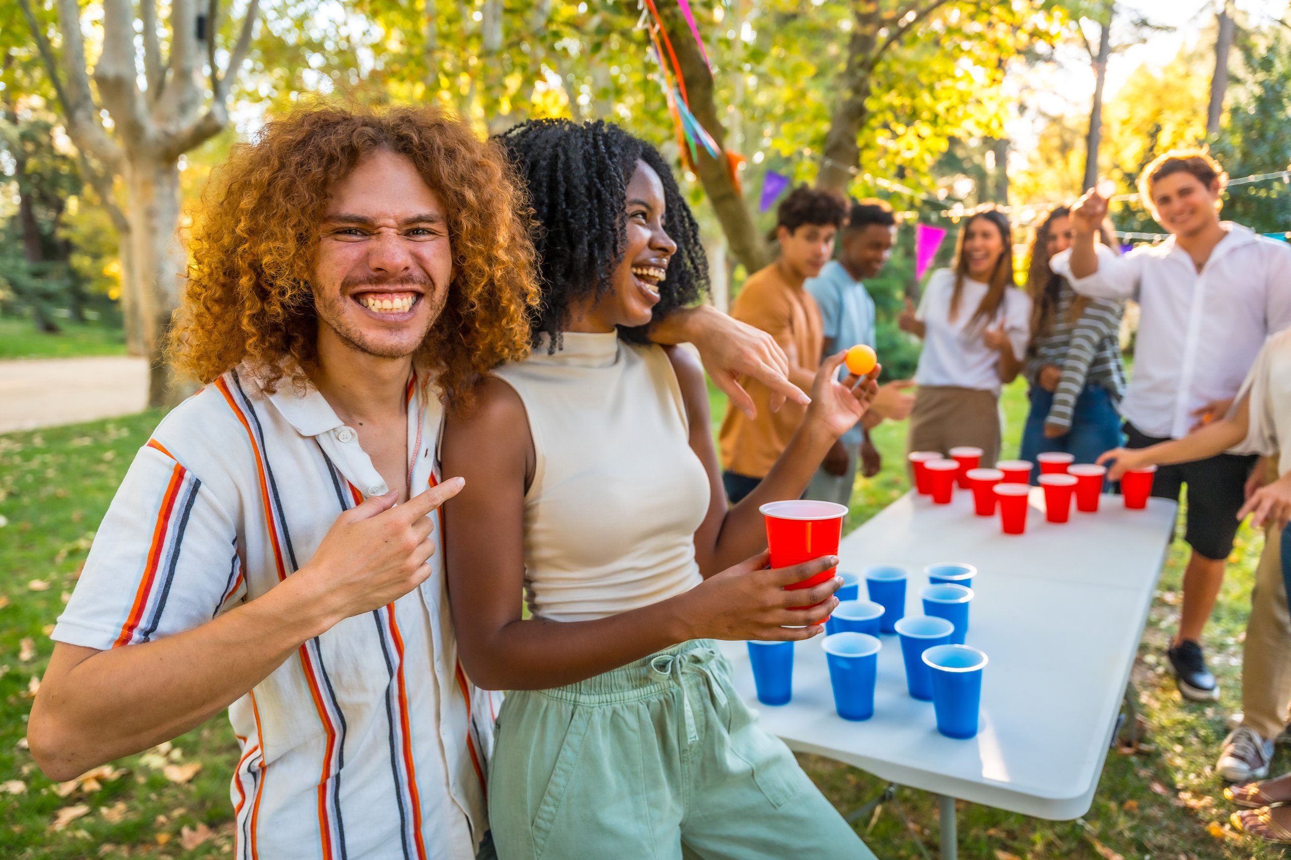Cheerful friends enjoying a beer pong game at an outdoor party