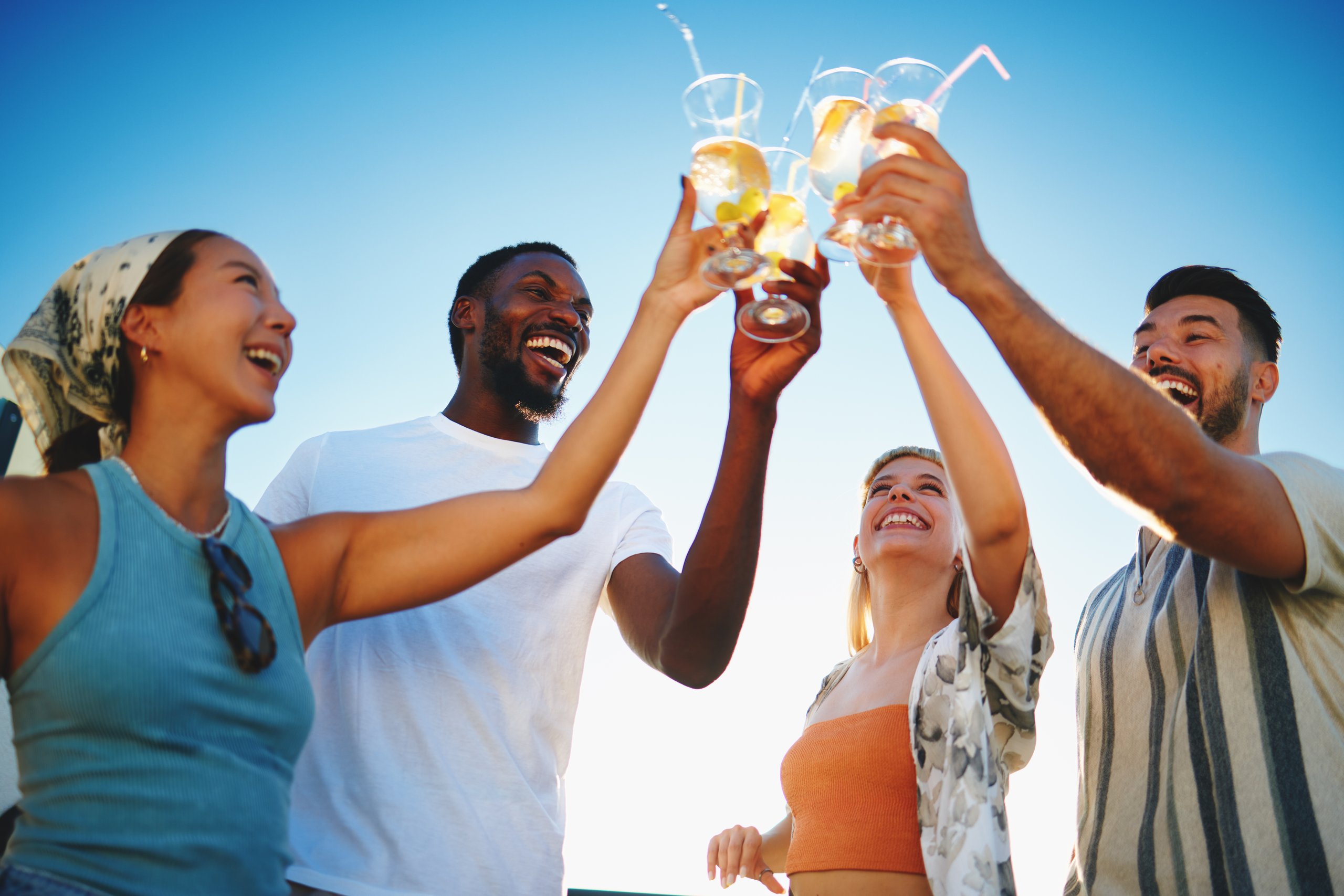 Cheerful multi-ethnic friends enjoying a rooftop party toasting with cocktails during summer vacation