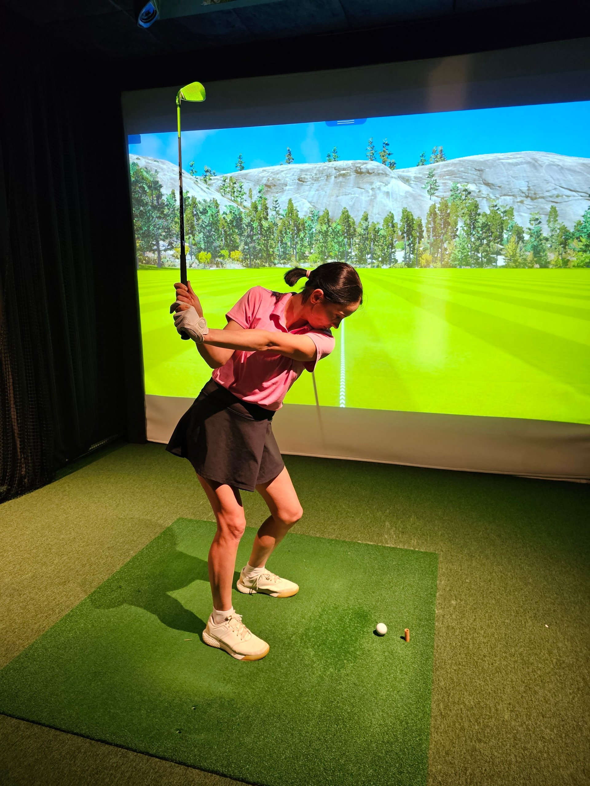Golfer prepares to swing in indoor simulator at sports facility